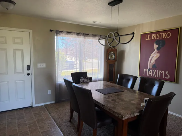 Transitional dining space featuring a modern linear chandelier, window with sheer treatments, and a patterned tile entry