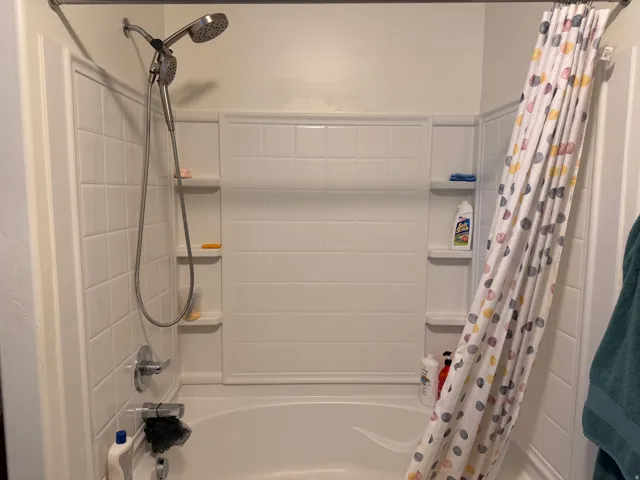 Bathtub and shower combination with white tile surround and built-in shelving