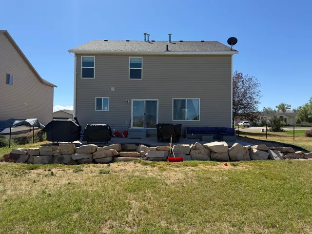 Rear exterior with a concrete patio, sliding glass door, and stone retaining wall