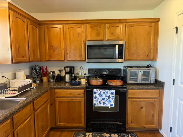 Full-height wood cabinetry with crown molding, stainless steel over-the-range microwave, built-in cooktop, and a corner sink