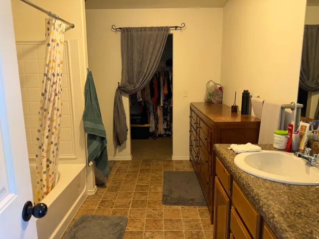 Bathroom with a built-in tub and shower combination, a vanity with an integrated sink, and an adjacent walk-in closet