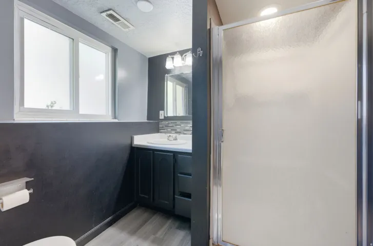 Bathroom featuring a white vanity sink, dark wood-finish cabinetry, mosaic tile backsplash, and a framed mirror