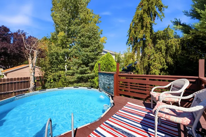 Expansive outdoor deck with a private swimming pool, wood railing, and surrounding mature trees