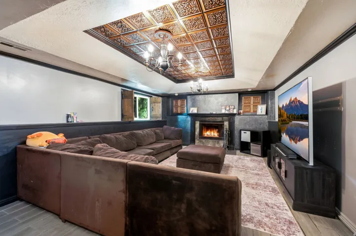 Coffered ceiling with decorative panels, built-in fireplace with a stone surround, and wood-finish flooring