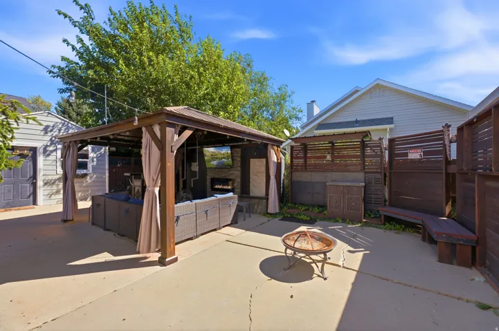 Concrete patio featuring a built-in gazebo with drapes, an exterior fireplace, and a fire pit