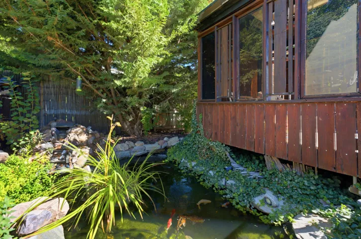 Wood-sided exterior with large windows, featuring a natural rock waterfall, koi pond, and lush landscaping