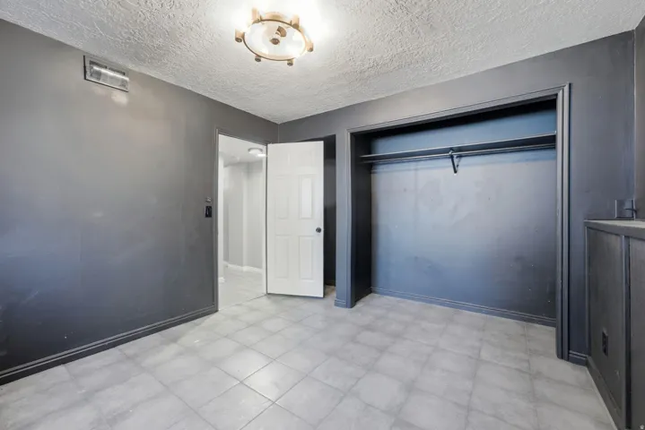 Interior room featuring light-colored tile flooring, a built-in closet with shelving and a hanging rod, and a ceiling-mounted light fixture