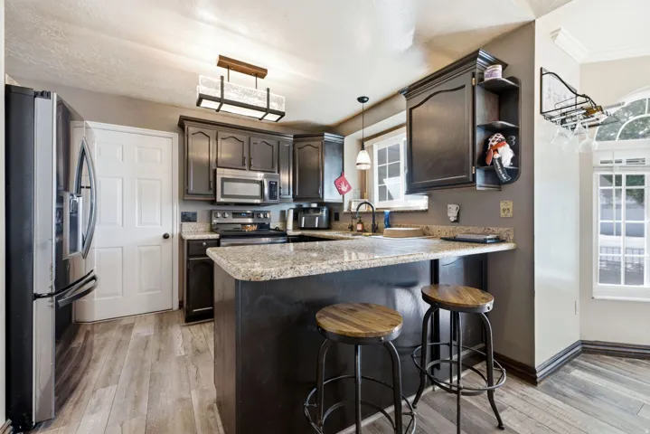 Kitchen featuring wood-finish flooring, dark cabinetry, stainless steel appliances, a breakfast bar, and a single-basin sink with a gooseneck faucet
