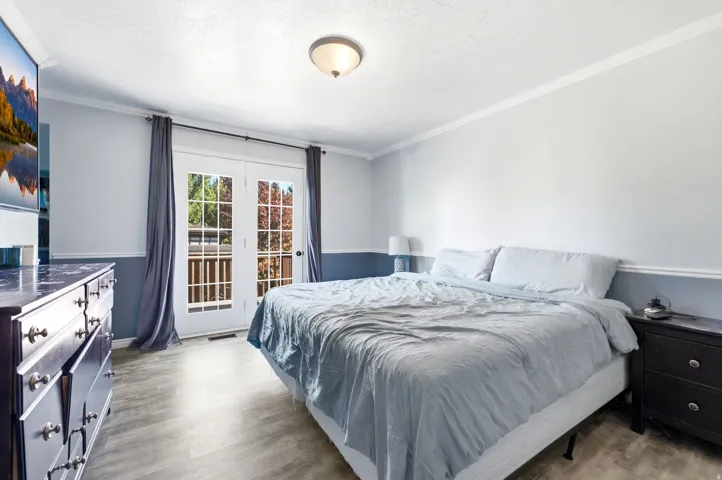 Wood-finish flooring, two-tone wall treatment, crown molding, double French doors, and ceiling-mounted light fixture