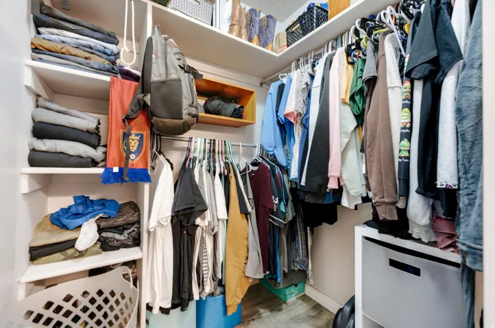 Built-in white shelving, wood-finish flooring, and integrated hanging rods for garment storage