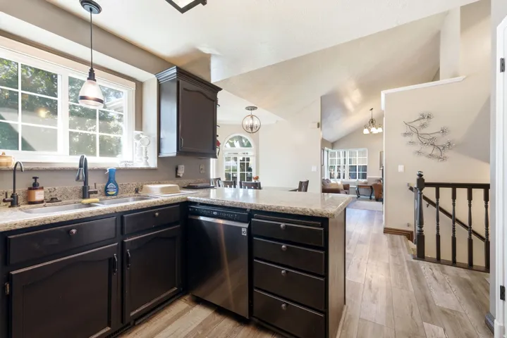 Kitchen featuring dark wood cabinetry, light granite countertops, stainless steel dishwasher, and wood-finish flooring