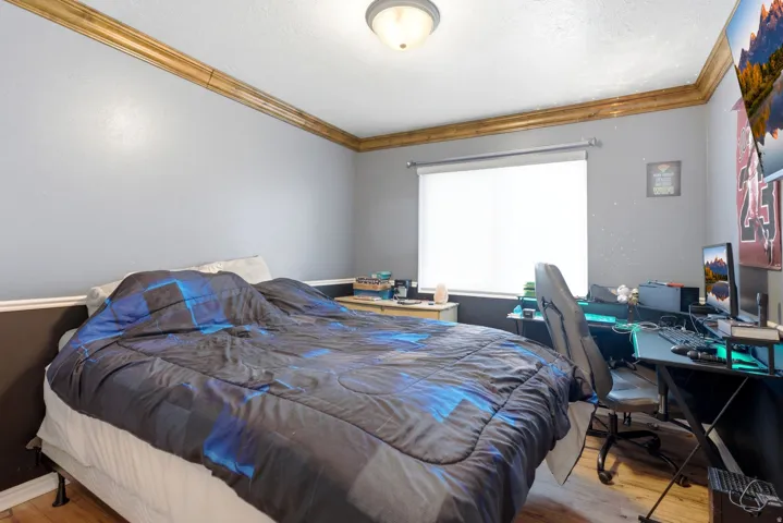 Recessed window with roller shade, wood-finish flooring, two-tone wall paint, and wood crown molding