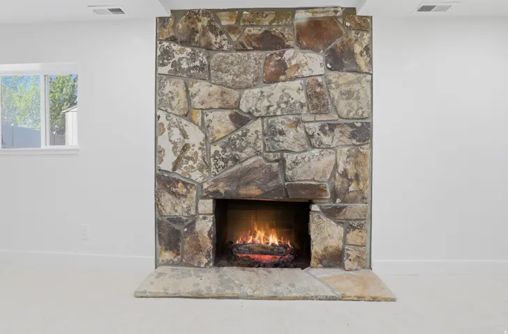 Stone-clad fireplace with a hearth, set against white walls and light-colored carpeting