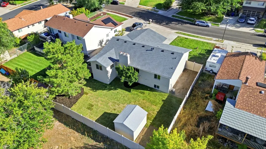 Expansive property featuring a grey shingle roof, light-colored siding, multiple mature trees, a white perimeter fence, and a storage shed