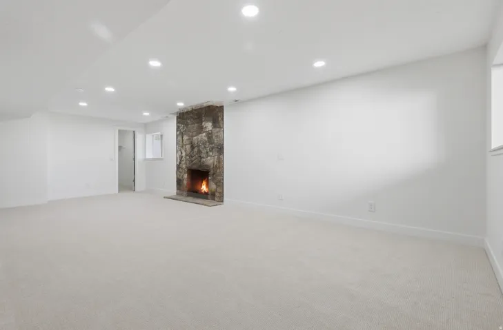 Expansive carpeted room featuring a stone fireplace, recessed lighting, and a window providing natural illumination