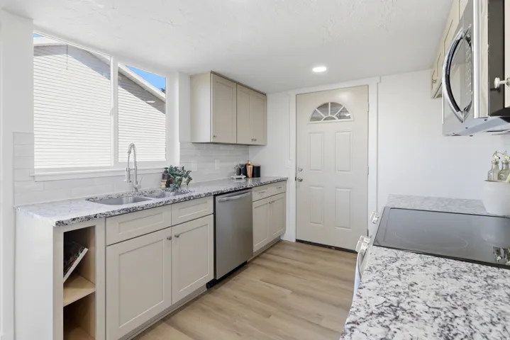 Contemporary kitchen with wood-finish flooring, light cabinetry, granite countertops, and stainless steel appliances
