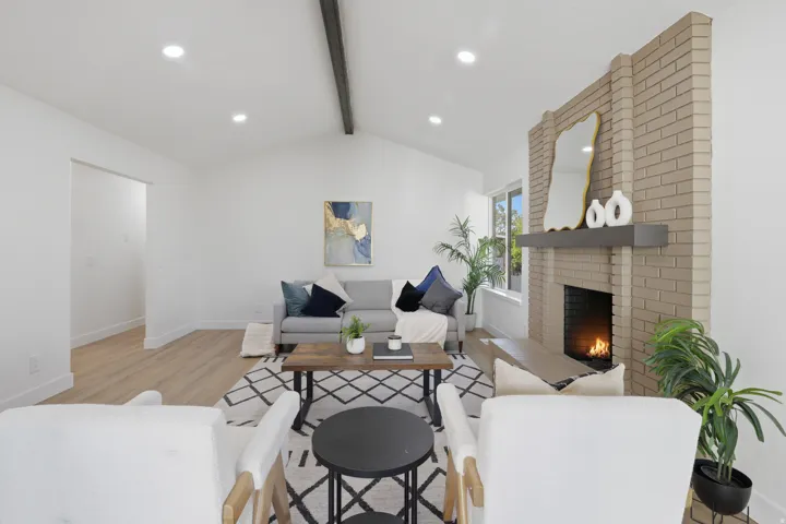 Vaulted ceiling with exposed beam, recessed lighting, brick fireplace with mantel, and wood-finish flooring