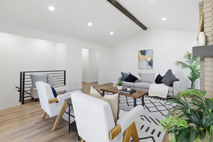Vaulted ceiling with exposed beam, recessed lighting, wood-finish flooring, brick fireplace with mantel, and black metal railing