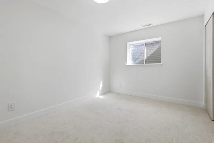 Light-colored carpeting, white painted walls, and a single window with blinds