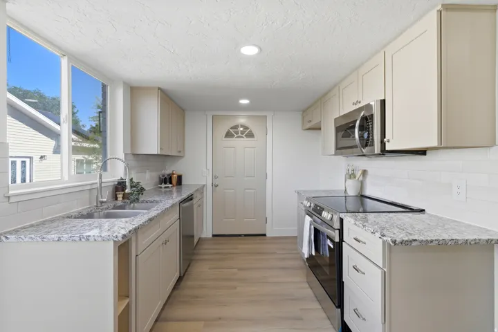 Spacious kitchen featuring light-toned cabinetry, light-toned countertops, a stainless steel sink, wood-finish flooring, and a stainless steel oven with a matching microwave