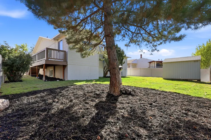 Rear exterior featuring a wooden deck with dark brown railing, light-colored siding, a large grassy area, and a storage shed