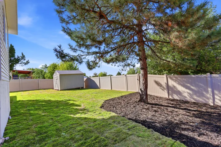 Manicured lawn, mature tree, garden shed, privacy fencing, and wood chip landscaping