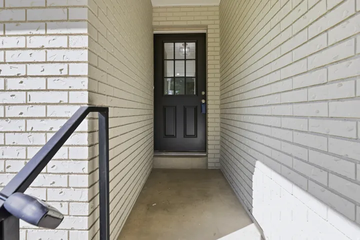 Entryway with white brick exterior, black paneled door with glass inserts, and a metal handrail