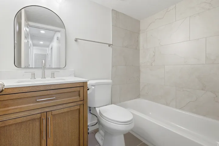 Wood-tone vanity with white countertop, chrome faucet, and arched mirror