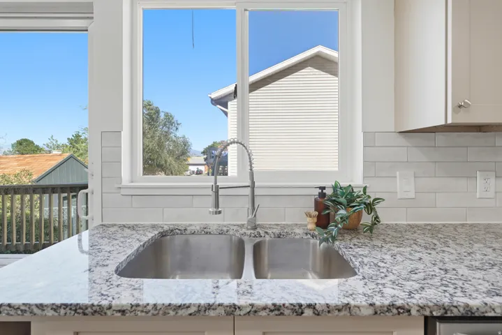 Dual basin stainless steel sink, pull-down faucet, granite-style countertops, white subway tile backsplash, and upper cabinetry