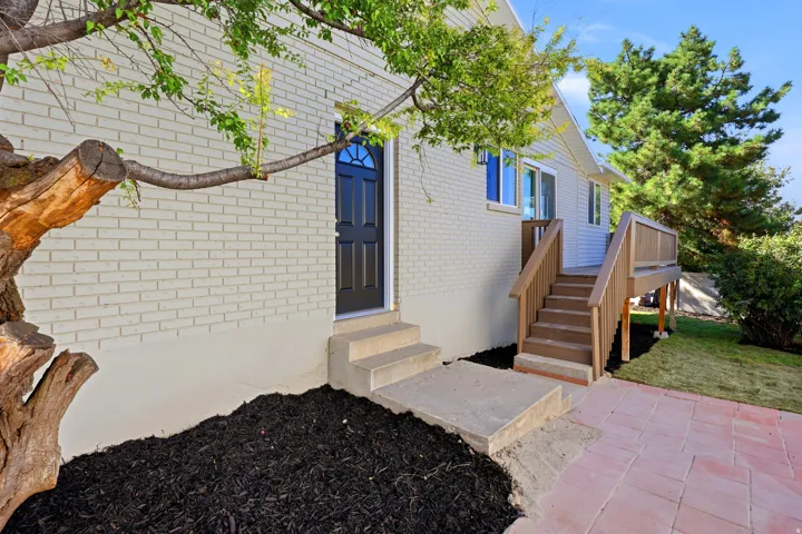 Brick exterior, black paneled entry door with transom detail, concrete entry stairs, wood deck with railing, and stamped concrete patio