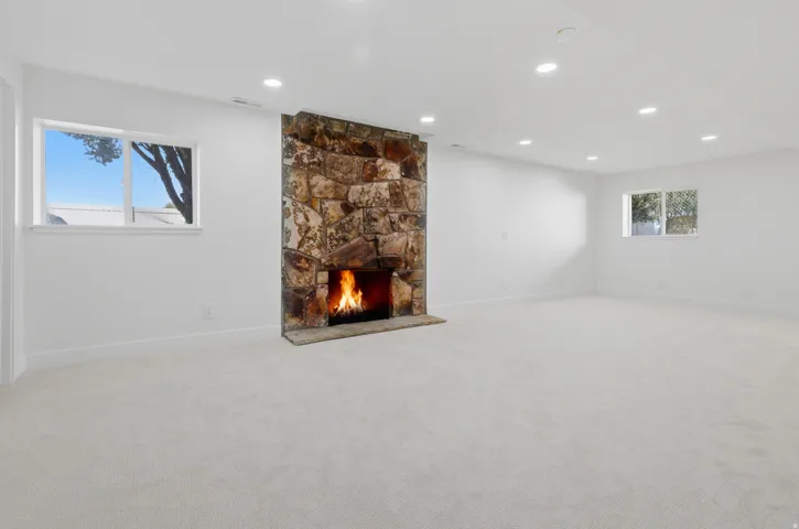 Stone-clad fireplace with a hearth, recessed lighting, white walls, and light-colored carpeting