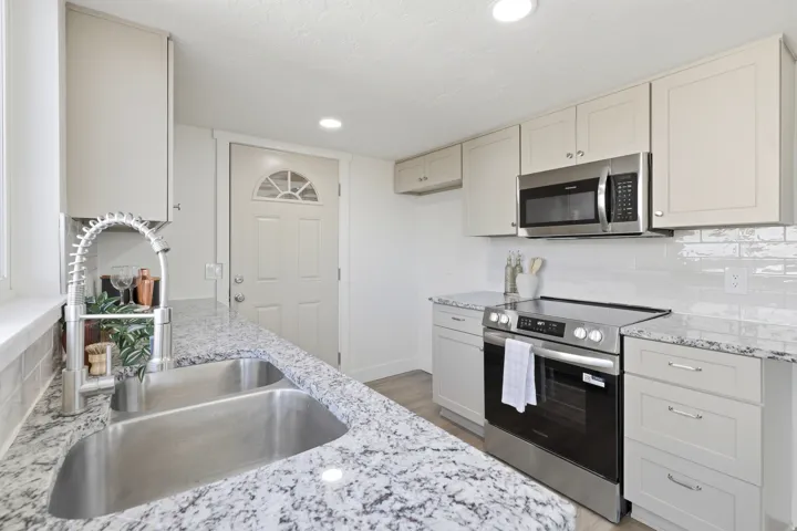 Modern kitchen featuring light-toned cabinetry, stainless steel appliances, granite-style countertops, a white subway tile backsplash, and recessed lighting