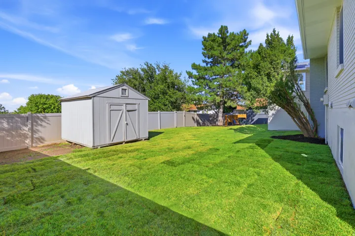 Expansive fenced backyard featuring a manicured lawn, a detached storage shed, and mature perimeter trees