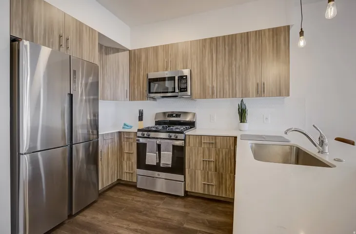 Modern kitchen featuring stainless steel appliances, wood-finish cabinetry, white countertops, and a white tiled backsplash