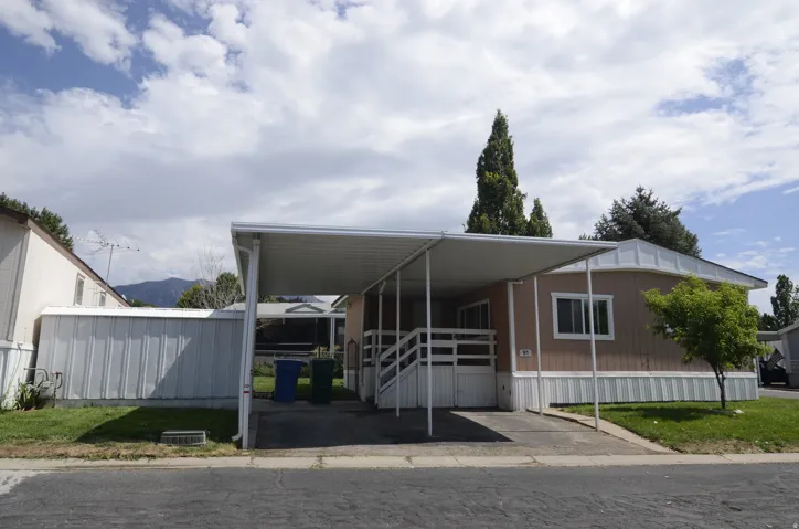 Carport structure, white railing, tan siding, white trim, and a paved driveway