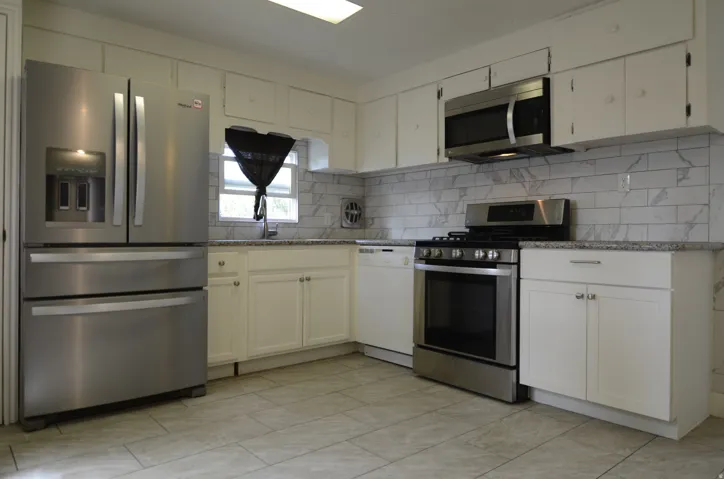 Kitchen featuring stainless steel appliances, white cabinetry, a tile backsplash, light countertops, and tile flooring