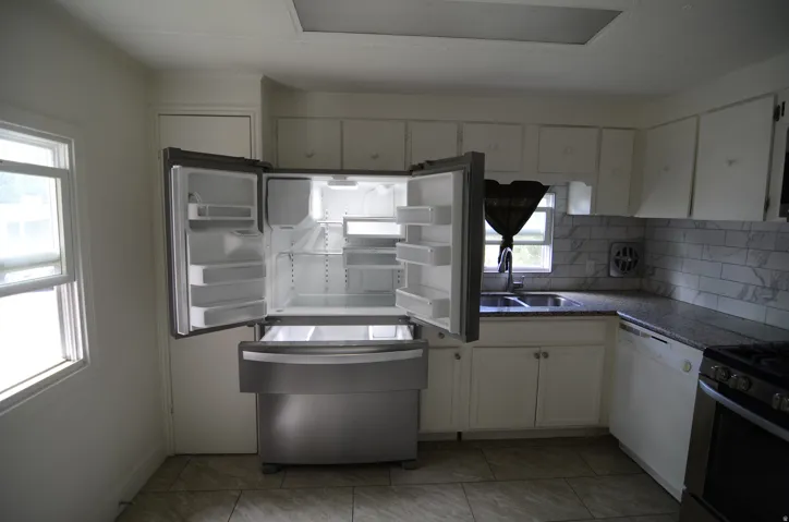 Kitchen featuring a stainless steel refrigerator, white cabinetry, dark speckled countertops, a tile backsplash, and a double basin sink with a gooseneck faucet