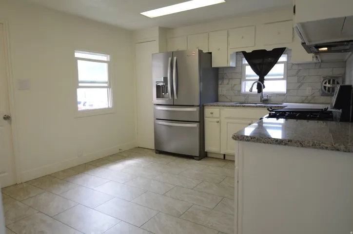 Kitchen featuring granite countertops, a tile backsplash, tile flooring, white cabinetry, and stainless steel appliances