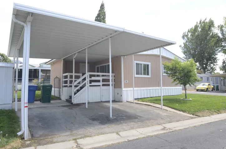 Carport structure, concrete driveway, exterior siding, white trim, and a small tree