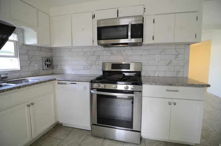 Kitchen featuring white cabinetry, granite countertops, tile backsplash, stainless steel range, and an integrated microwave