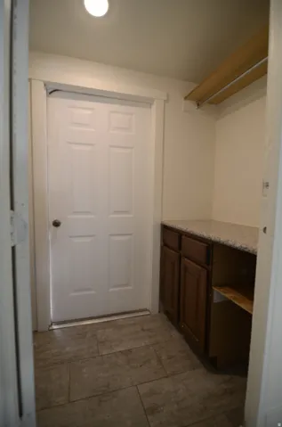 Tile flooring, white paneled door, built-in cabinetry with solid surface countertop, and overhead shelving