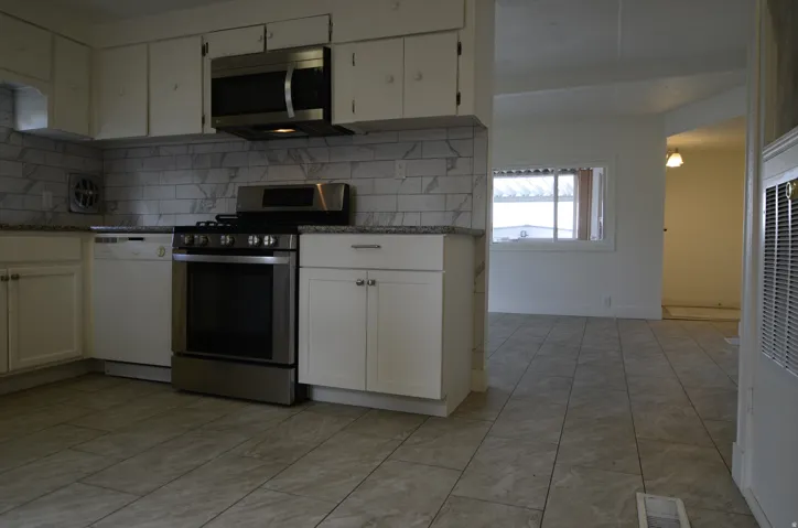 Kitchen featuring stainless steel appliances, white cabinetry, tile backsplash, and granite-style countertops
