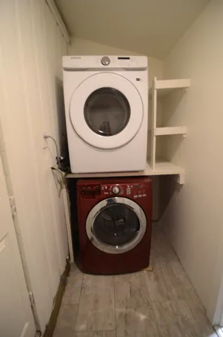 Laundry area featuring a stacked washer and dryer, wood-finish flooring, and built-in shelving
