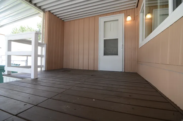 Covered porch featuring wood flooring, vertical siding, a storm door, exterior lighting, and a window