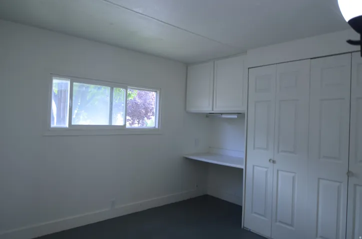 Built-in desk with overhead cabinetry, under-cabinet lighting, dual bi-fold closet doors, and white trim