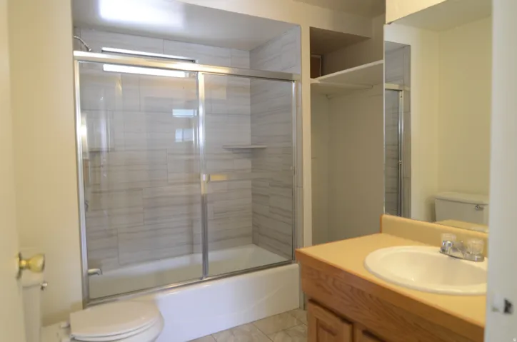 Tub-shower combination with sliding glass doors, tiled surround, built-in shelving, and a vanity with an integrated sink