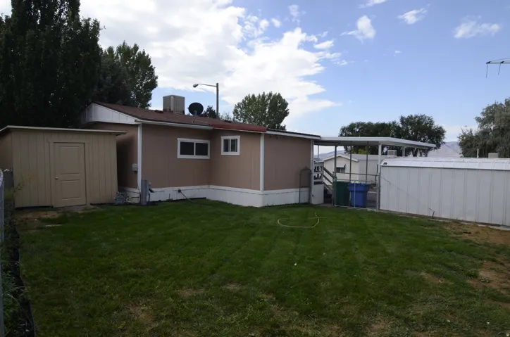 Expansive rear yard featuring green lawn, a detached storage shed, and an attached carport