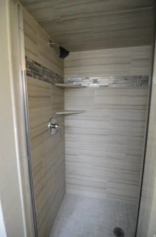 Tiled shower enclosure featuring a mosaic accent band, two corner shelves, and a chrome shower fixture