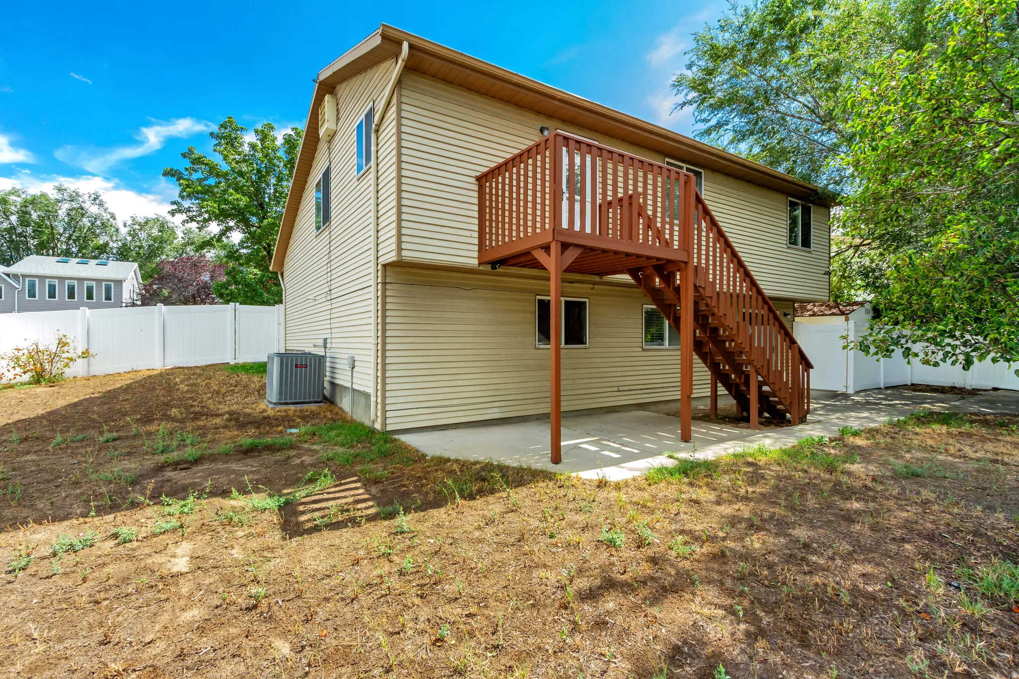 Two-story exterior with light-colored siding, featuring a brown wood-finish deck and stairs