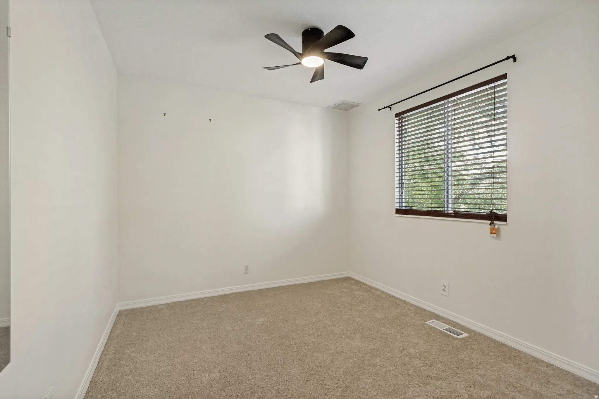 White wall finishes, carpeted flooring, window with blinds, ceiling fan with integrated lighting